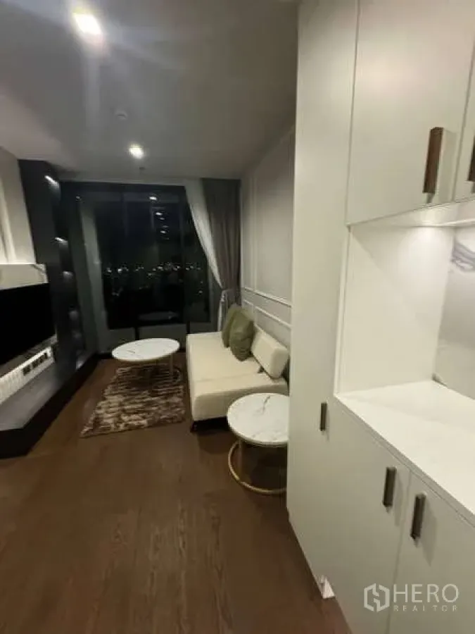 Condominium for rent in Khlong Toei, Bangkok - Open-plan living room view from the entry with built-in cabinetry and balcony access.