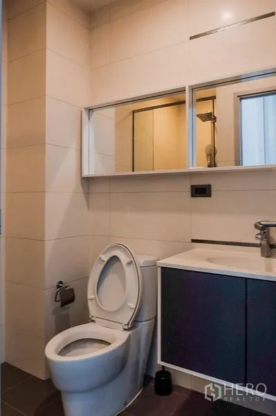 Condominium for rent in Khlong Toei, Bangkok - Second bathroom with toilet, under-sink cabinet and wide mirror.