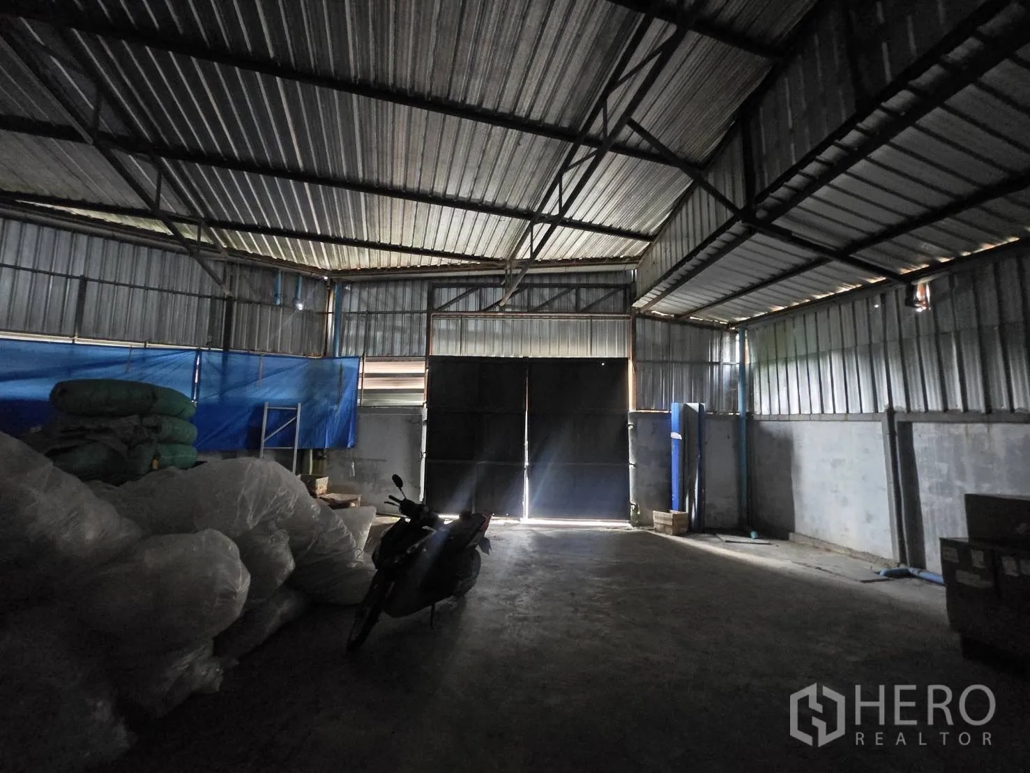 Factory for rent or sale in Mueang Samut Sakhon, Samut Sakhon - Dim warehouse section with double metal doors and exposed steel truss roof.