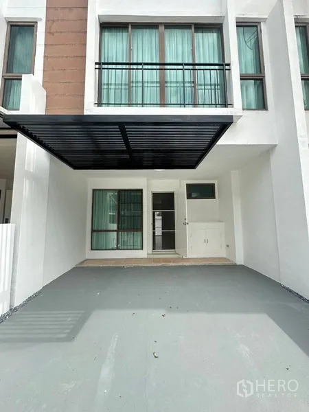 Townhouse for rent or sale in Phra Khanong, Bangkok - Covered carport and entrance with large windows and green curtains.