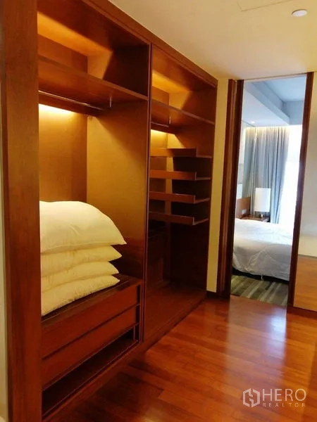 Condominium for rent in Pathum Wan, Bangkok - Walk-in closet with built-in wooden shelves, drawers and soft lighting.