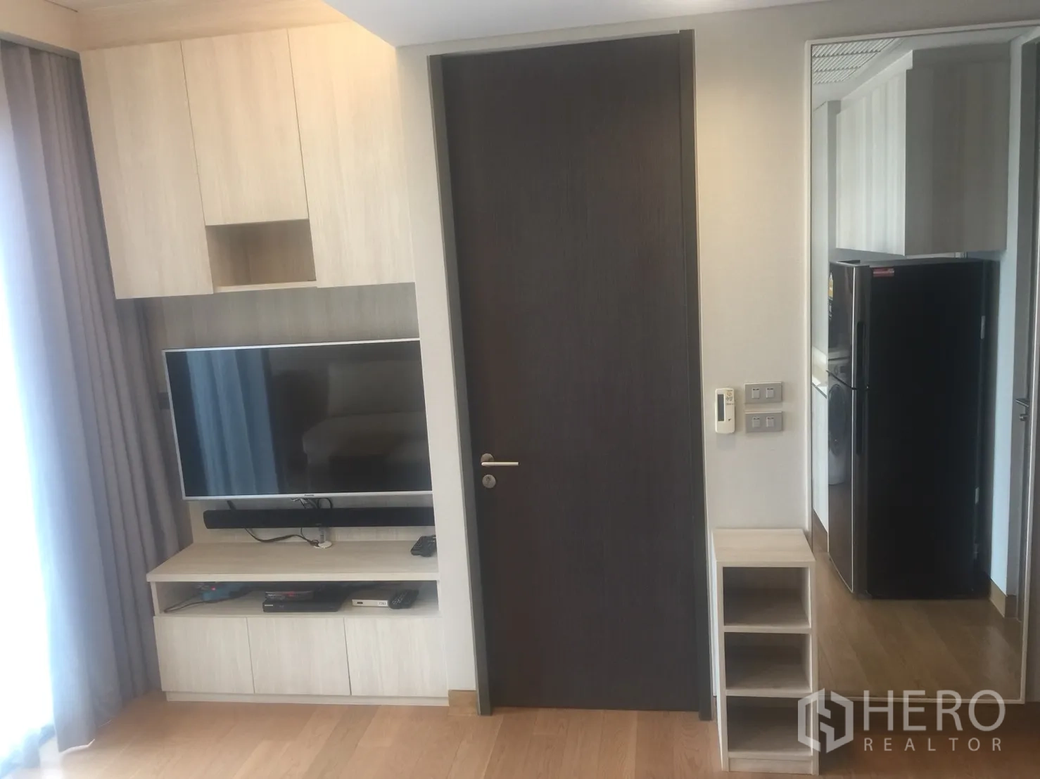 Condominium for rent in Khlong Toei, Bangkok - Living room TV wall with built-in storage, flat-screen TV, and dark wood door.