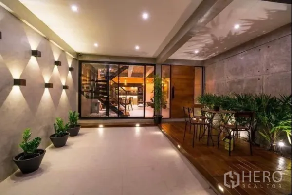 Townhouse for rent in Khlong Toei, Bangkok - Covered terrace with wall lights, potted greenery and sliding glass doors opening to the living area.