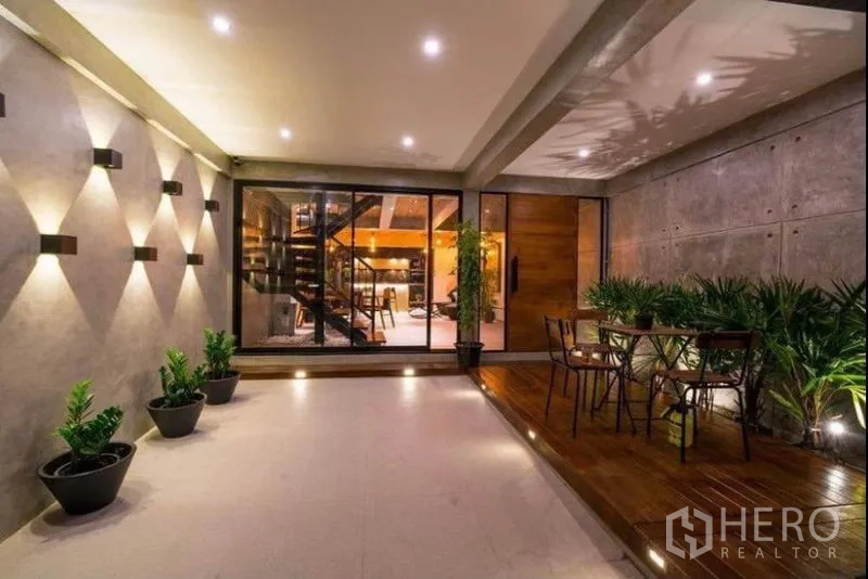 Townhouse for rent in Khlong Toei, Bangkok - Covered terrace with wall lights, potted greenery and sliding glass doors opening to the living area.
