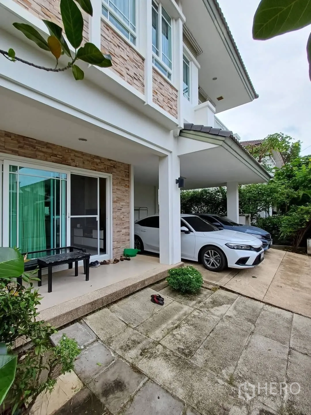 Detached House for sale in Bang Kapi, Bangkok - Side exterior with covered terrace, stone cladding and two parked cars.