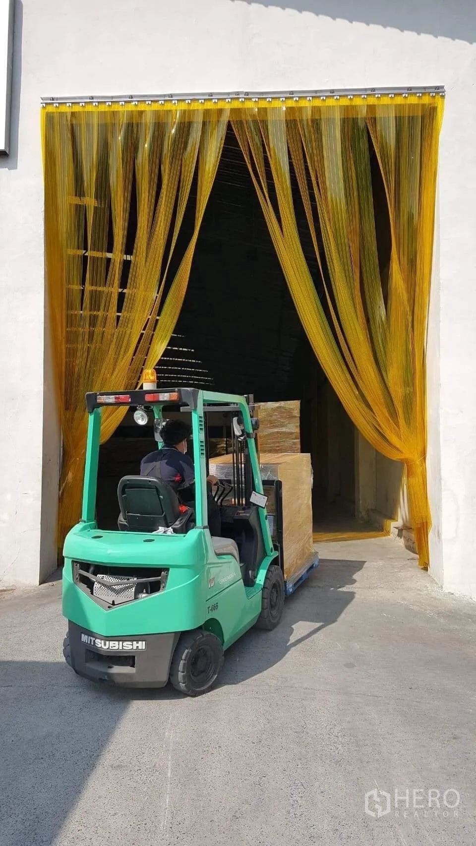 Factory for rent or sale in Pathum Thani - Forklift moving a pallet through yellow PVC strip curtain at a loading bay.