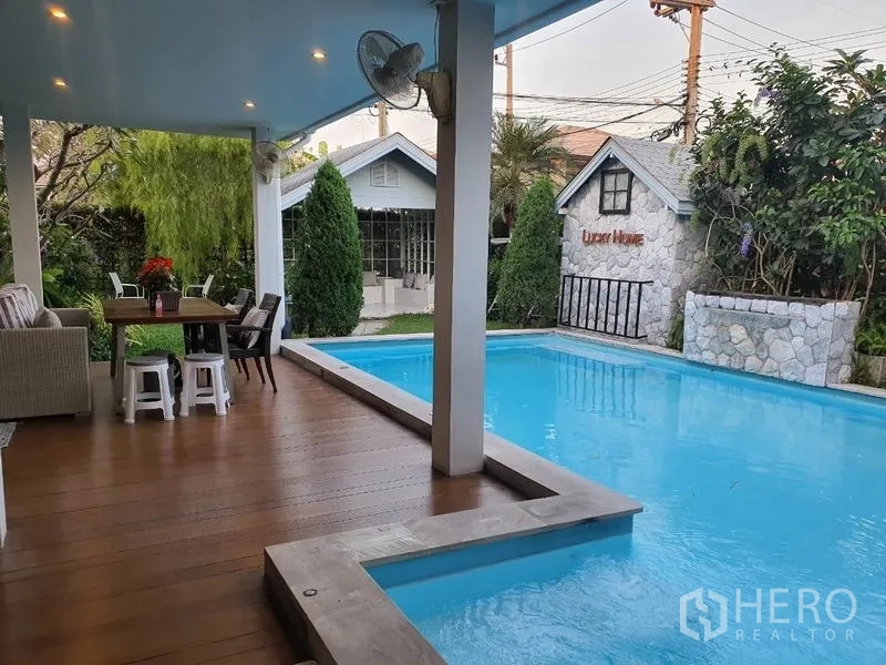 Detached House for sale in Lam Luk Ka, Pathum Thani - Private swimming pool beside a covered deck with ceiling fans, stone feature wall and greenery.