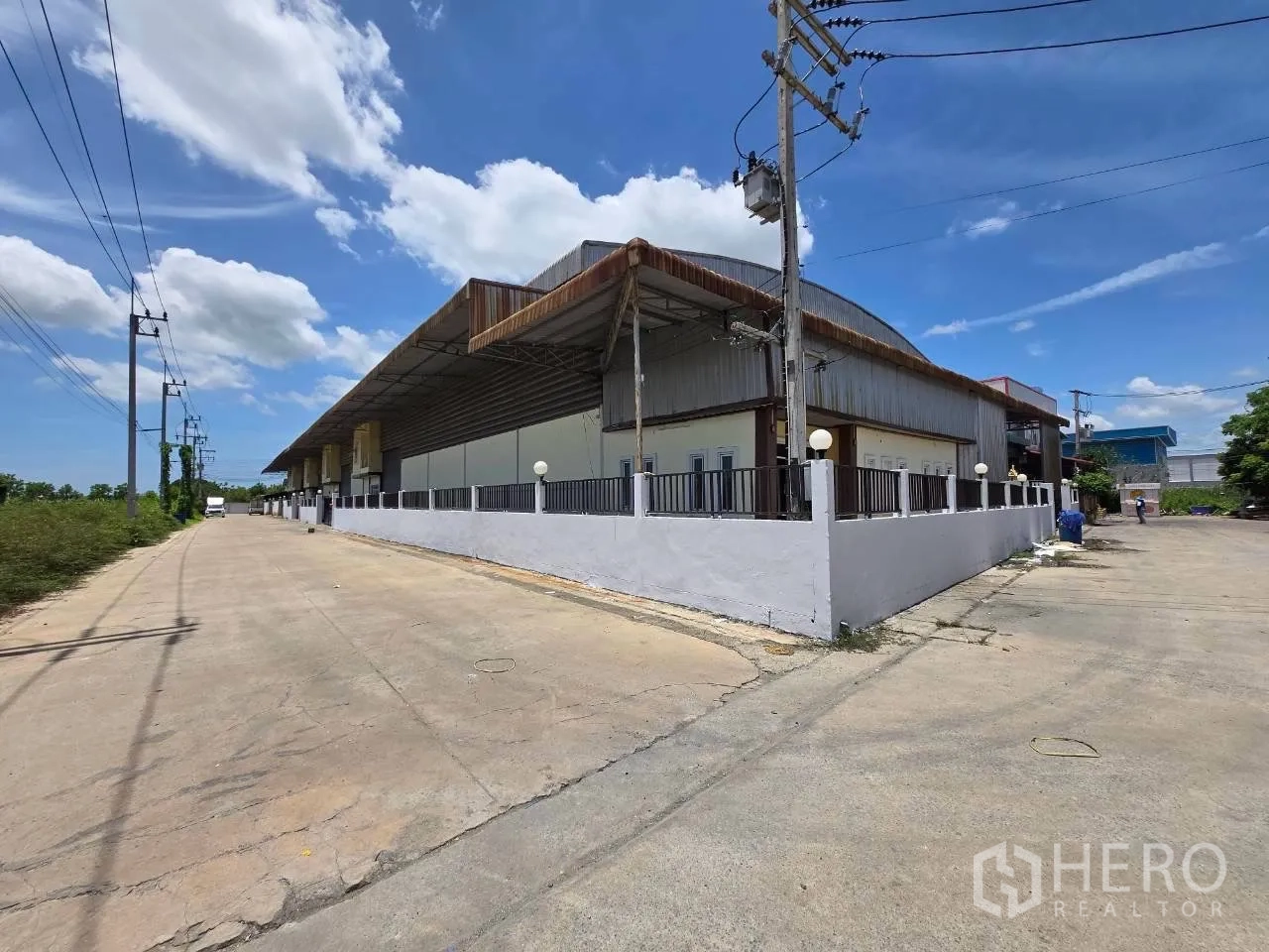 โกดัง for rent or sale in Mueang Samut Sakhon, Samut Sakhon - ภาพมุมถนนแสดงรั้วรอบโกดังและถนนทางเข้าโล่งกว้าง