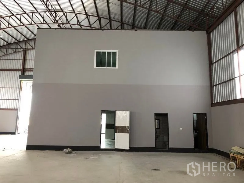 Factory for rent or sale in Bang Len, Nakhon Pathom - Close view of the internal office block with multiple doors and a window beneath steel truss roofing.