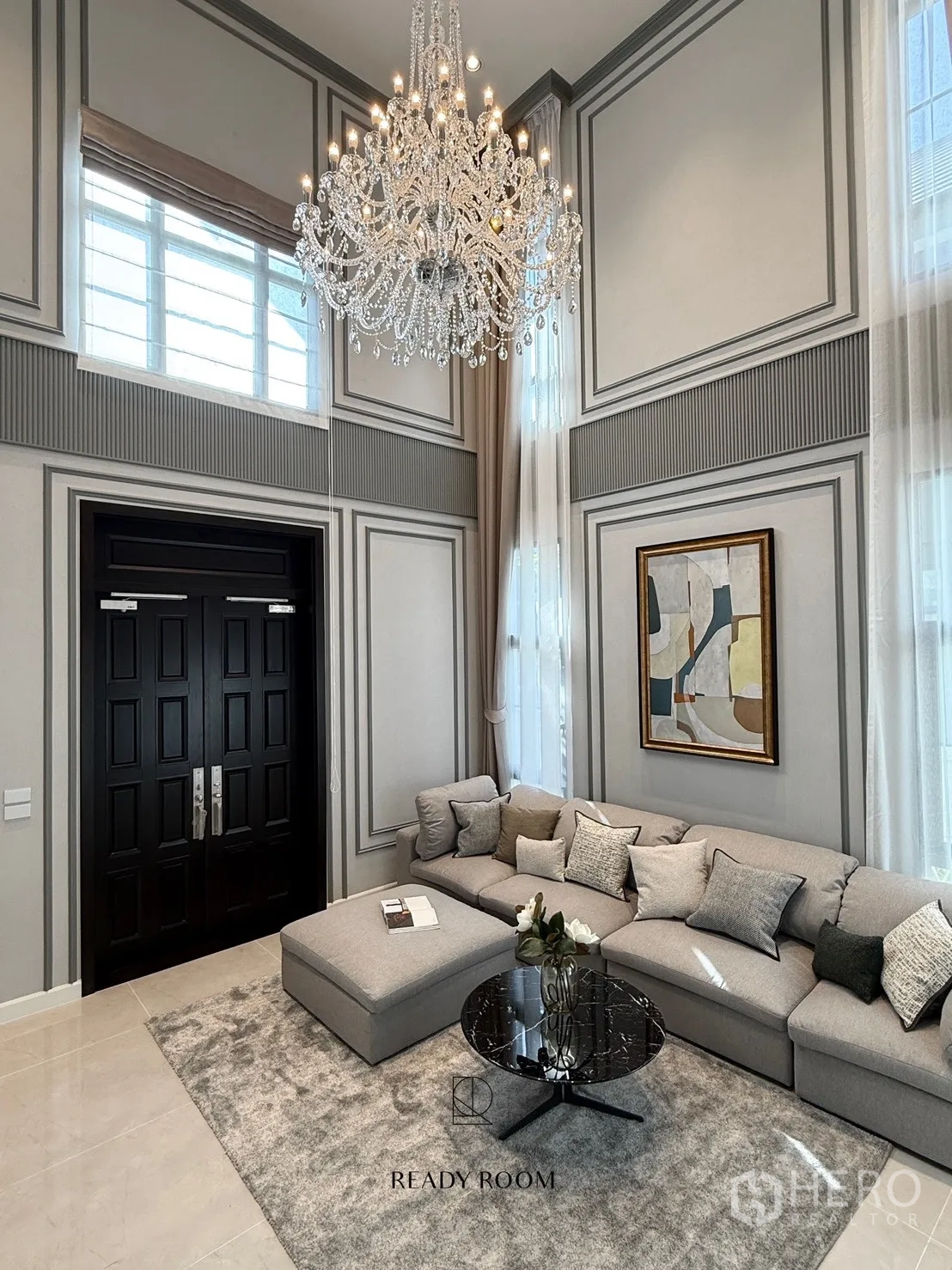 Detached House for rent or sale in Bang Phli, Samut Prakan - Double-height living room with grand crystal chandelier, tall windows and a large grey sectional sofa.