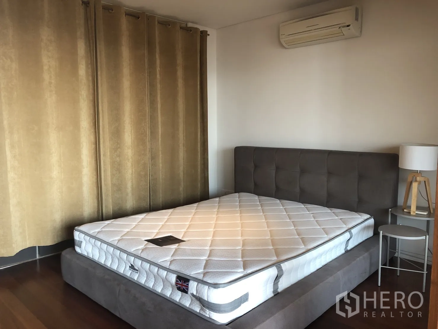 Condominium for rent in Pathum Wan, Bangkok - Cozy bedroom with upholstered bed base, new mattress, bedside table and lamp, air conditioner, and blackout curtains.