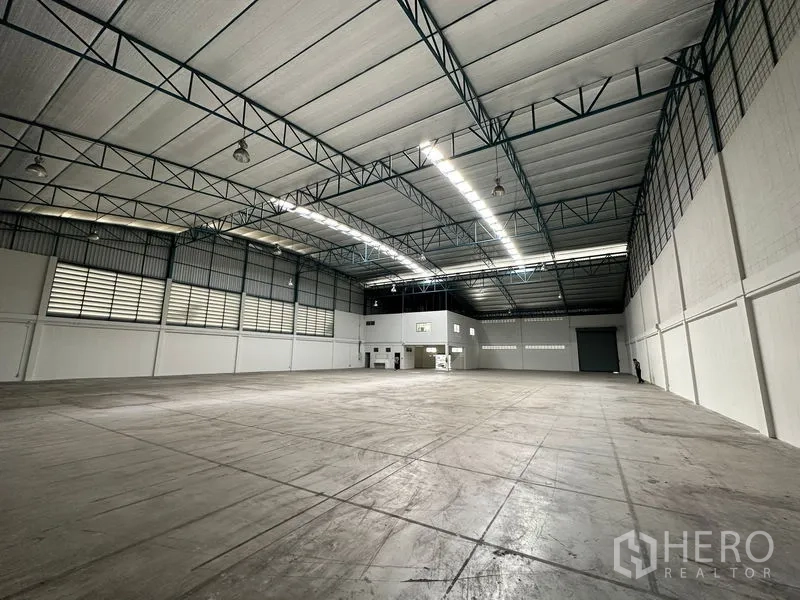 Factory for rent in Si Racha, Chon Buri - Expansive warehouse hall with high steel-truss ceiling, skylight strips, smooth concrete floor, office block and a large roller shutter.