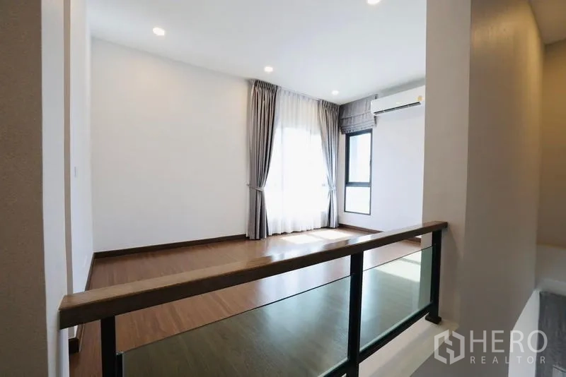 Detached House for rent in Bang Phli, Samut Prakan - Upper landing with wood flooring and glass railing near large windows.