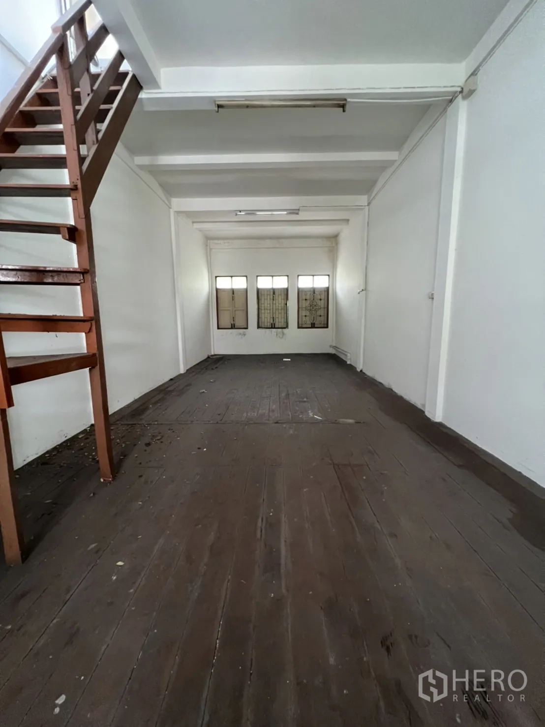 Shophouse for rent in Khlong Toei, Bangkok - Upper floor space with timber flooring, three front windows with grilles, white ceiling beams and side staircase.