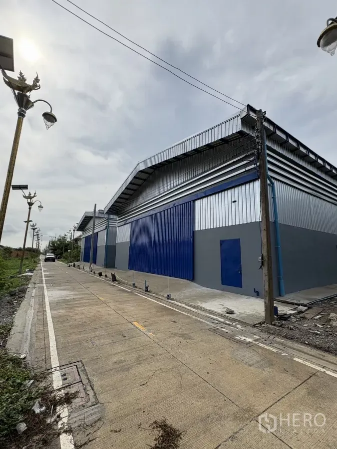 货栈 出租在Bang Phli, Samut Prakan - Bang Phli 仓库外观，蓝灰金属立面，临路通行宽敞并设混凝土停车区。