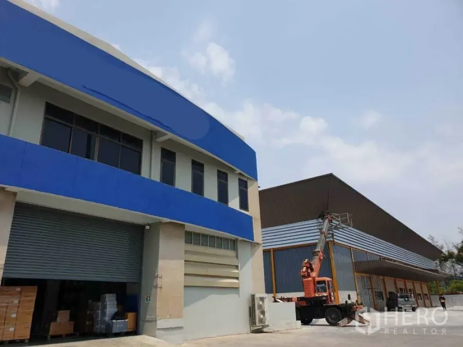 工厂 出租在Bang Pakong, Chachoengsao - 工厂外观，带蓝色两层办公室、卷闸装卸口与作业中的臂式升降车。