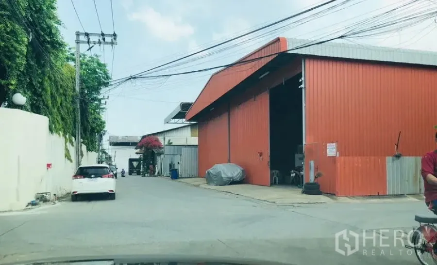 Warehouse for rent in Bueng Kum, Bangkok - Street view of a red metal warehouse with a wide entrance on a quiet industrial lane in Nawamin, Bangkok.