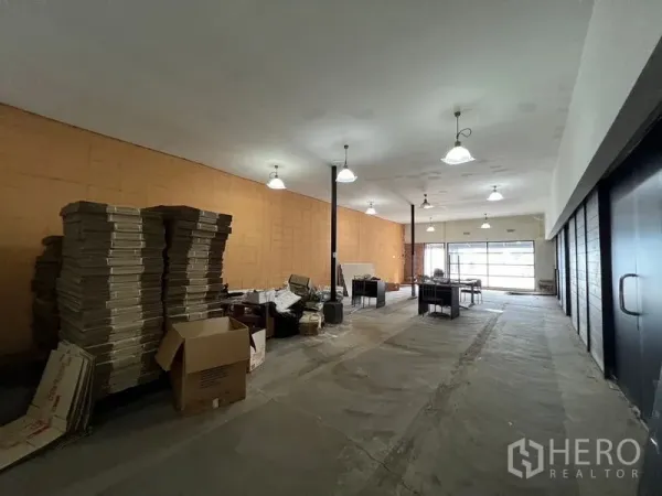 Warehouse for rent in Suan Luang, Bangkok - Open-plan warehouse interior featuring high ceilings, pendant lights, concrete flooring, and front glazing with stacked cartons.