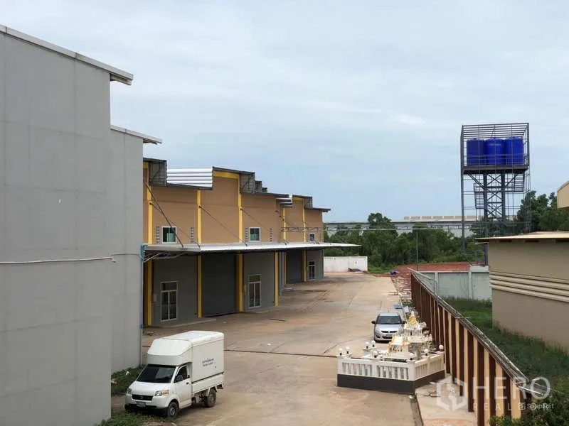 Factory for rent in Mueang Samut Sakhon, Samut Sakhon - Factory compound driveway with parking areas, water tank tower, and multiple warehouse bays.