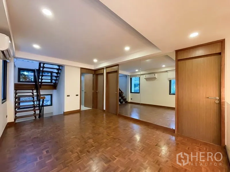 Townhouse for rent in Khlong Toei, Bangkok - Flexible upper-floor room with mirrored wall, wood floors, and stair access.