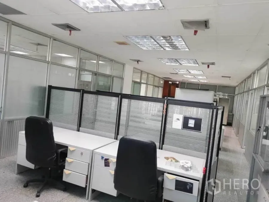 Office Space for rent in Bang Na, Bangkok - Workstations with divider screens, swivel chairs, and overhead fluorescent lighting in a glass-partitioned office.