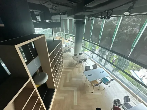 Office Space for rent - Aerial view of double-height office showing curved floor-to-ceiling windows, worktables and leafy street outlook.