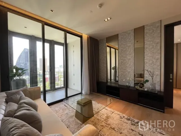 Condominium for rent in Khlong Toei, Bangkok - Modern living room with floor-to-ceiling sliding doors to the balcony, mirrored feature wall, and city view.