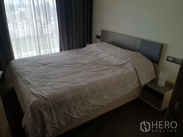 Condominium for rent in Pathum Wan, Bangkok - Cozy bedroom with double bed and sheer curtains revealing a city view.