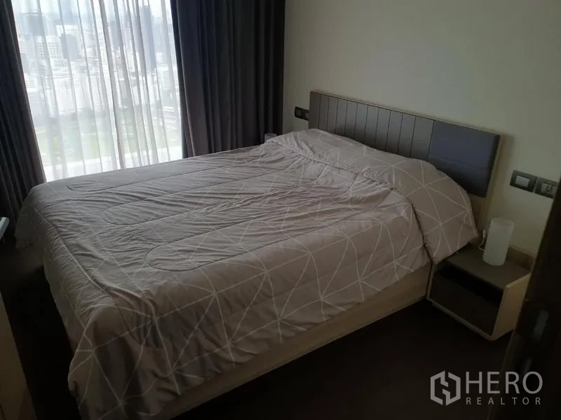 Condominium for rent in Pathum Wan, Bangkok - Cozy bedroom with double bed and sheer curtains revealing a city view.