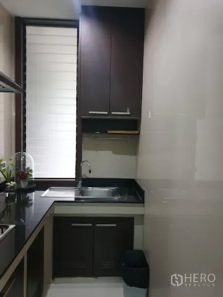 Detached House for sale in Watthana, Bangkok - Kitchen sink corner with dark cabinetry and tall window.