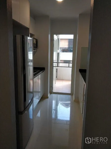 Condominium for rent in Khlong Toei, Bangkok - Sleek galley kitchen with glossy cabinets, black countertops, and access to a small balcony.