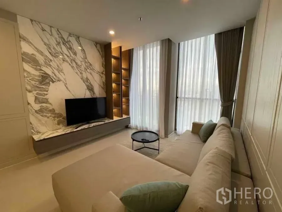 Condominium for rent in Pathum Wan, Bangkok - Living room with L-shaped sofa, marble-feature TV wall and full-height windows.