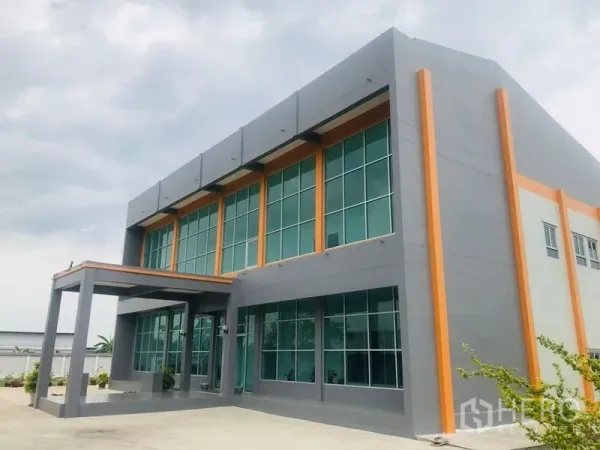 Factory for sale in Bang Sao Thong, Samut Prakan - Front corner view of a newly built factory with a two-storey glass-front office and orange trims.