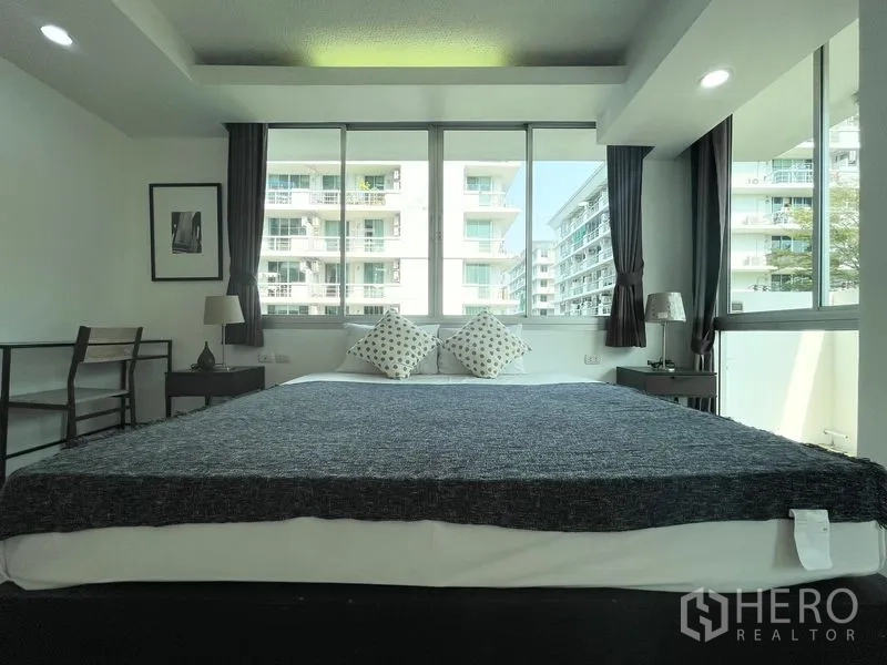 Condominium for rent in Khlong Toei, Bangkok - Front view of bedroom with king bed under expansive windows and curtains.