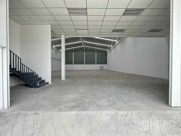 工厂 出租在Khlong Luang, Pathum Thani - 高挑仓库内部，混凝土地面，侧边楼梯通往夹层办公室。
