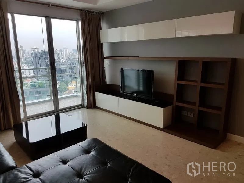 Condominium for rent in Khlong Toei, Bangkok - Bright living room with leather sofa, TV wall unit, and sliding doors opening to a balcony with Bangkok city views.