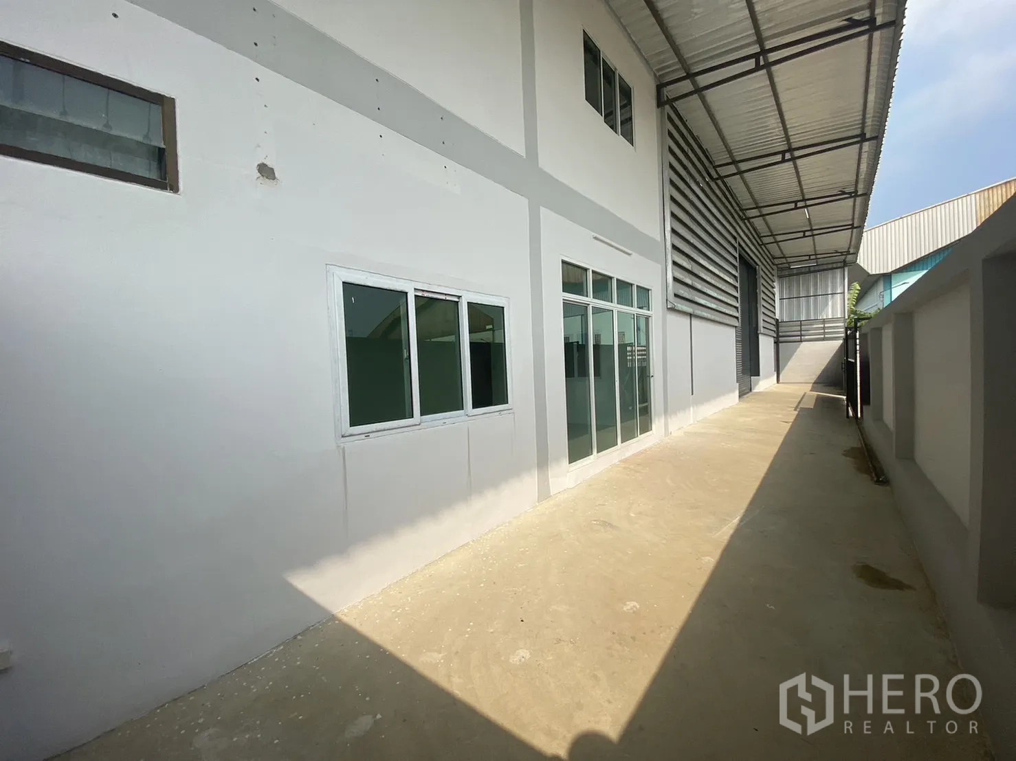 Factory for rent or sale in Mueang Samut Sakhon, Samut Sakhon - Glass-fronted office and windows along a side yard under a metal canopy.