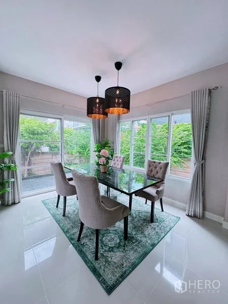Detached House for rent in Prawet, Bangkok - Dining area with glass table, upholstered chairs, and pendant lights by windows.