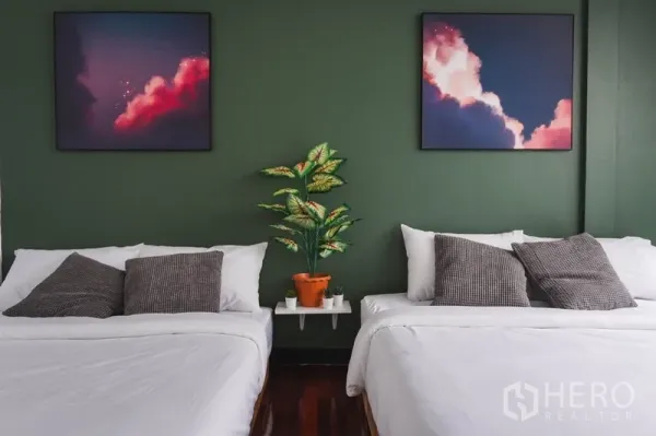 Townhouse for rent in Watthana, Bangkok - Bedroom with two beds, deep green feature wall, framed artwork and a potted plant.