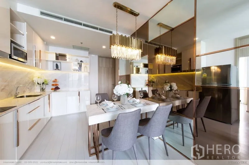 Condominium for rent in Pathum Wan, Bangkok - Dining zone with twin crystal pendants and mirrored wall beside a modern kitchen.