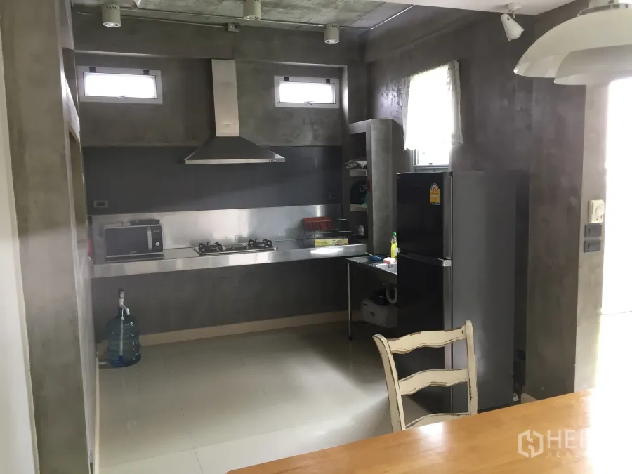 Townhouse for rent in Din Daeng, Bangkok - Modern concrete-style kitchen with stainless steel counters, gas hob, range hood, refrigerator and window light.