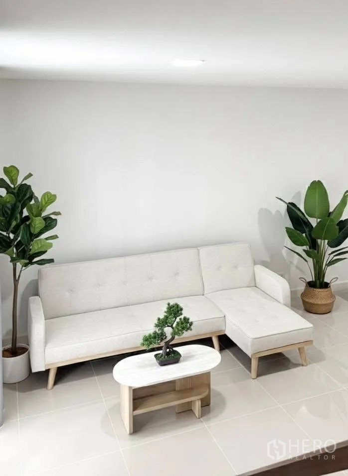 Townhouse for rent in Bang Phli, Samut Prakan - Cozy living corner with L-shaped sofa, small coffee table and potted plants on shiny tiles.