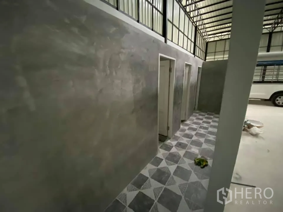Warehouse for rent in Saphan Sung, Bangkok - Utility corridor with concrete walls, doorways to rooms and patterned floor tiles inside the warehouse.