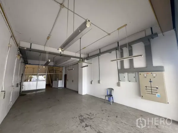 Warehouse for rent in Bang Phli, Samut Prakan - Ground-floor warehouse area with hanging fluorescent lights and electrical panels.
