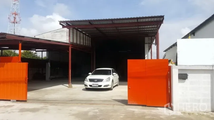 Warehouse for sale in Lam Luk Ka, Pathum Thani - Warehouse exterior with orange sliding gate, large concrete forecourt, covered loading bay and steel structure.