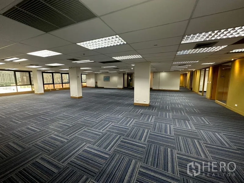 Office Space for rent in Khlong Toei, Bangkok - Blue-carpeted open office with columns and full-height windows.