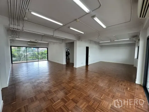 Office Space for rent in Watthana, Bangkok - Spacious work area with exposed conduit lighting, wood floors and wide windows overlooking trees.