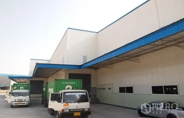 Factory for rent in Si Racha, Chon Buri - Covered loading bays with container trucks at a modern white-and-blue factory in Si Racha.
