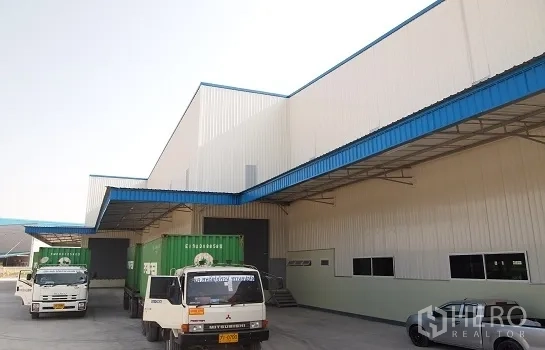 Factory for rent in Si Racha, Chon Buri - Covered loading bays with container trucks at a modern white-and-blue factory in Si Racha.