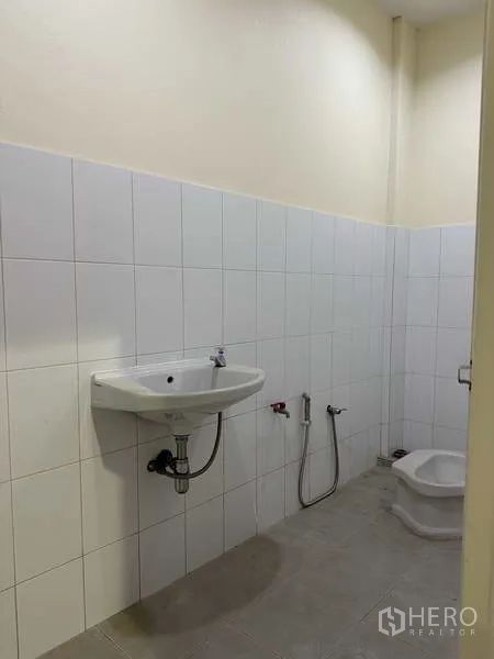 Factory for sale in Mueang Samut Prakan, Samut Prakan - Clean tiled restroom with wall-mounted sink and squat toilet fixtures.